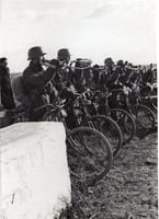 Soldiers on bicycles blow signaling horns and carry bouquets of flowers