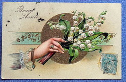 Antique embossed greeting card with a hand holding a lily of the valley flower on a gold background