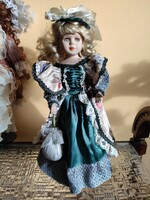 A doll with a porcelain head, a blonde curly lady in a green dress with lace frills and flowers