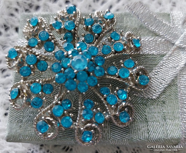 A beautiful brooch badge decorated with blue rhinestones embedded in a silver-plated metal alloy