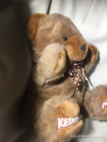 A big, long-furred teddy bear with a pocket on the back with the inscription 