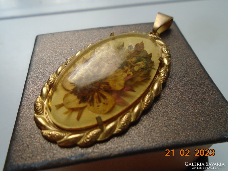 An oval dried flower pendant in a gilded frame with a porcelain back under a convex glass