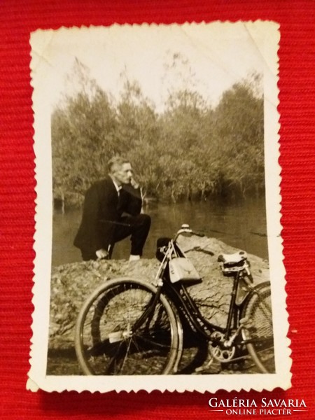 A man in an antique suit on the waterfront with a bicycle, small photo according to the pictures