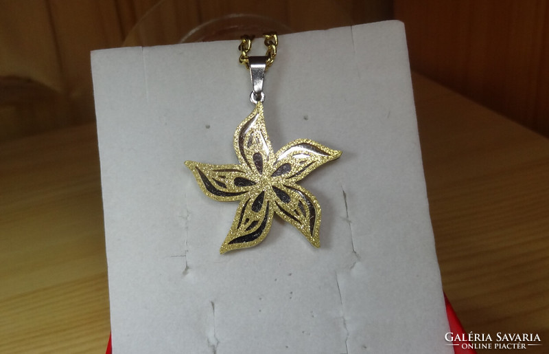 Pendant made of surgical steel in the shape of a flower with wavy petals. The surface of the flower is gold colored and grainy.