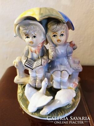 Porcelain sculpture, children sitting on a fence with umbrellas and geese