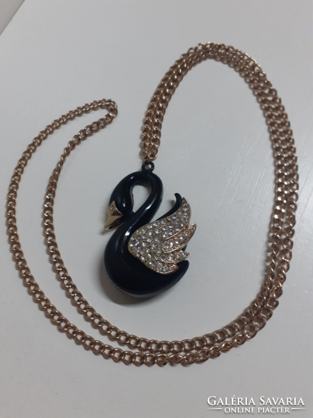 A long gold-colored chain in nice condition with a black swan on it, studded with many sparkling white stones
