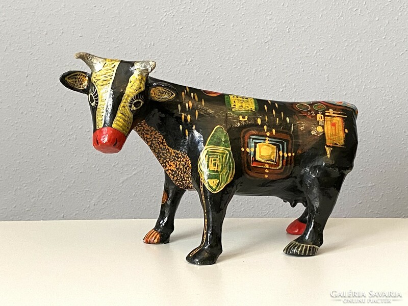 Paper mache cow sculpture with colorful modern abstract painting on a black background
