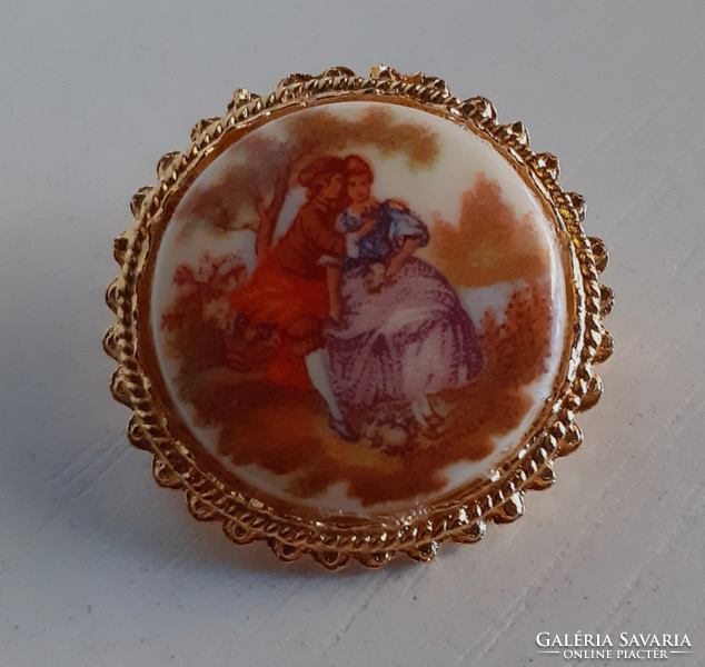 A brooch in a gilded frame with a porcelain scene stone