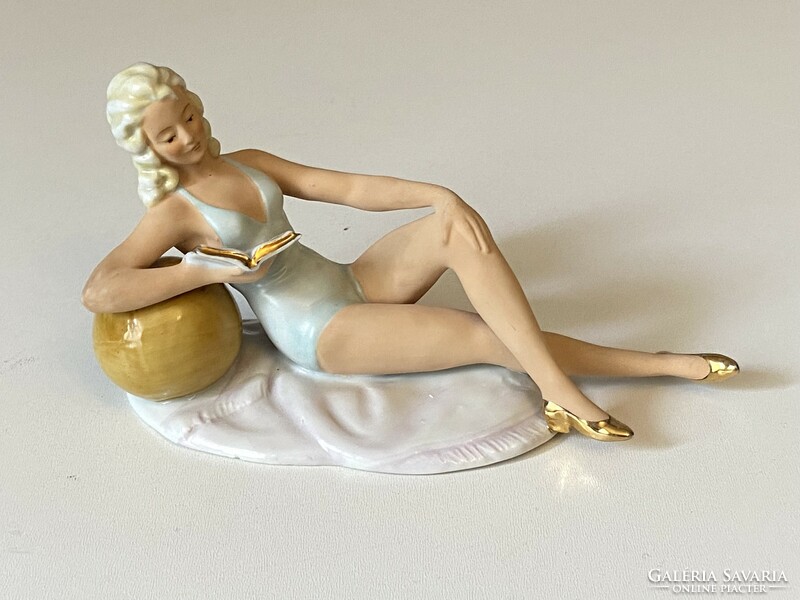 Painted German porcelain statue of a girl reading and sunbathing leaning on a ball
